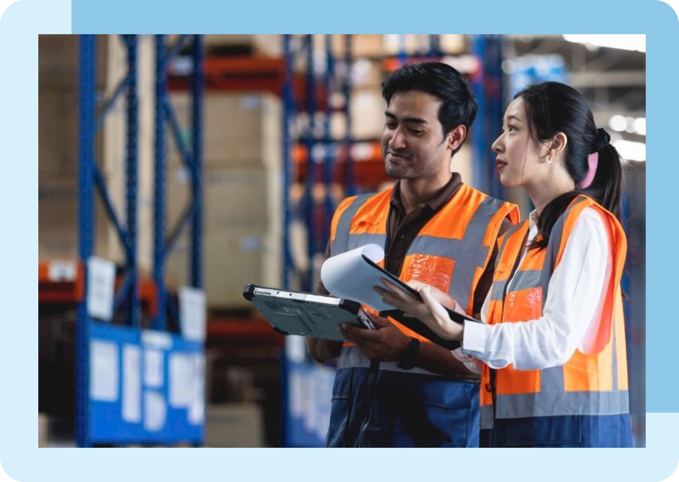 A man and woman wearing safety vests examine goods in a warehouse