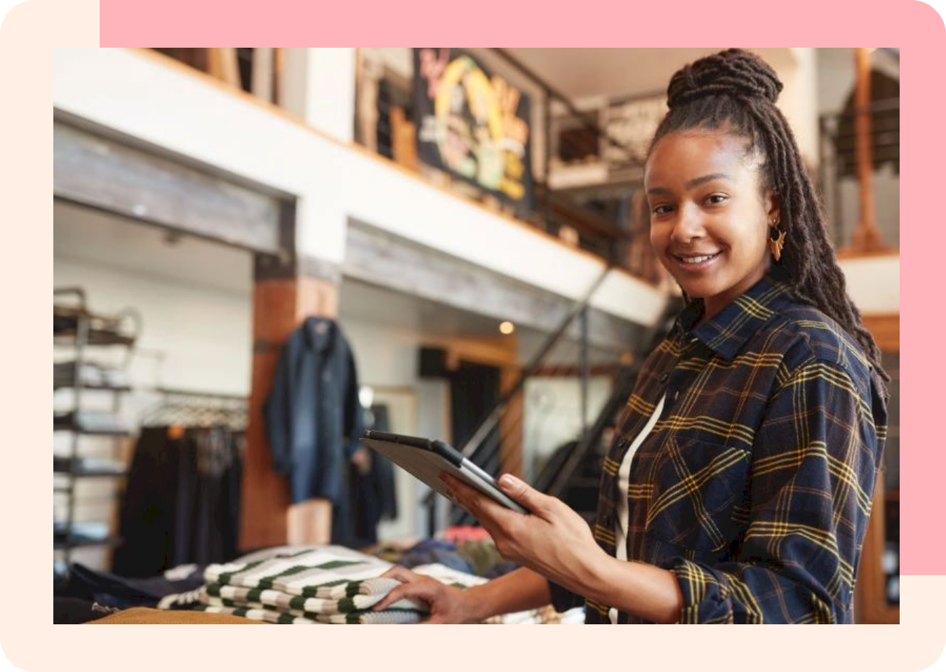 A young woman in a retail store holding a tablet in her left hand and touching a folded pile of shirts with her right